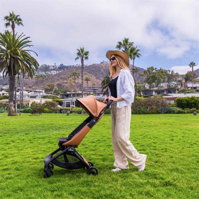 Mima Miro Compact Stroller in mocha cream with black chassis, pushed by a woman in casual attire in a park setting.