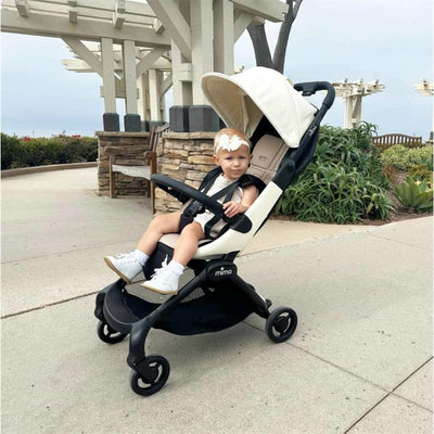 Mima Miro Compact Stroller with black chassis and white seat, featuring a toddler wearing a headband, outdoors.