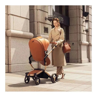 Mima Xari MAX stroller in champagne, black, and camel color being wheeled by a woman in a trench coat on a city sidewalk.