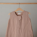 100% organic cotton muslin baby wearable blanket in a natural, soft beige color displayed on a wooden hanger.
