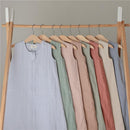 Organic cotton muslin baby wearable blankets in pastel shades hanging on a wooden rack.