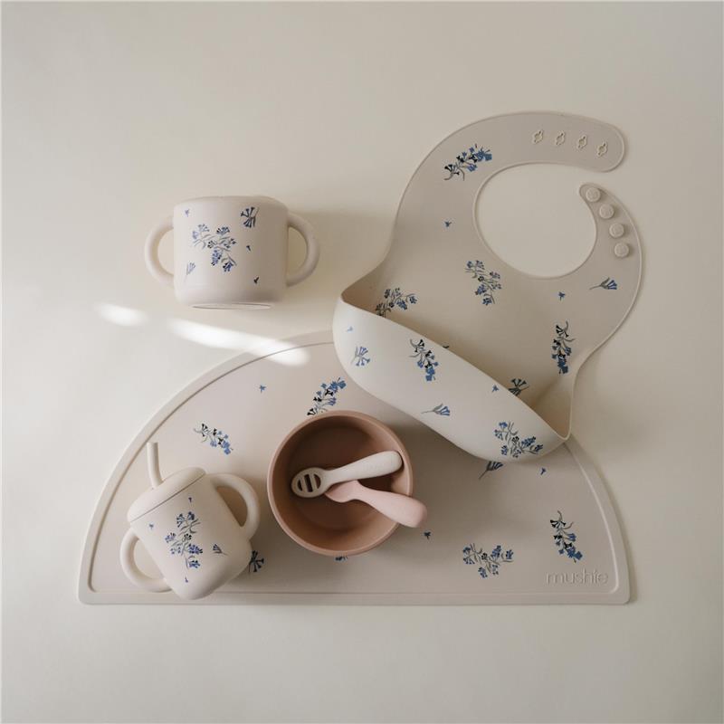 Silicone training cup with straw, bib, and bowl in lilac flowers design for toddlers, displayed on a soft surface.