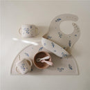 Silicone training cup with straw, bib, and bowl in lilac flowers design for toddlers, displayed on a soft surface.