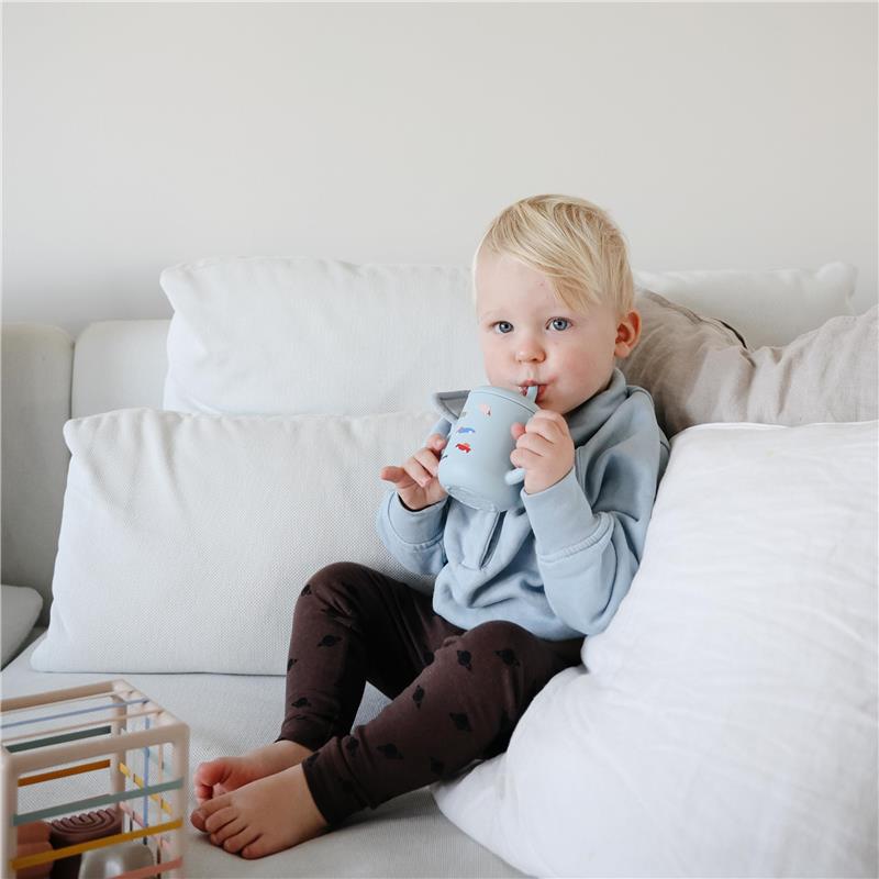 Toddler with blonde hair, wearing a light blue sweatshirt, sipping from a blue silicone training cup with planet designs.