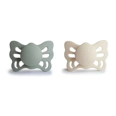 Two anatomical silicone pacifiers in cream and sage green colors, designed for infants aged 0-6 months, with a butterfly shape.