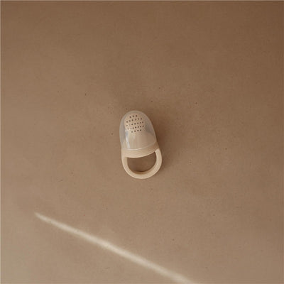 Silicone food feeder in shifting sand color, featuring a perforated top and a handle for easy grip.