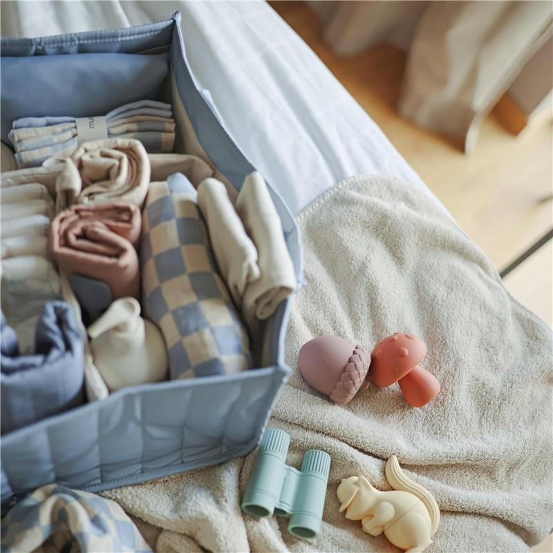 Mushie Baby Diaper Caddy in blue floral design, filled with neatly organized baby essentials, including clothes and soft toys.