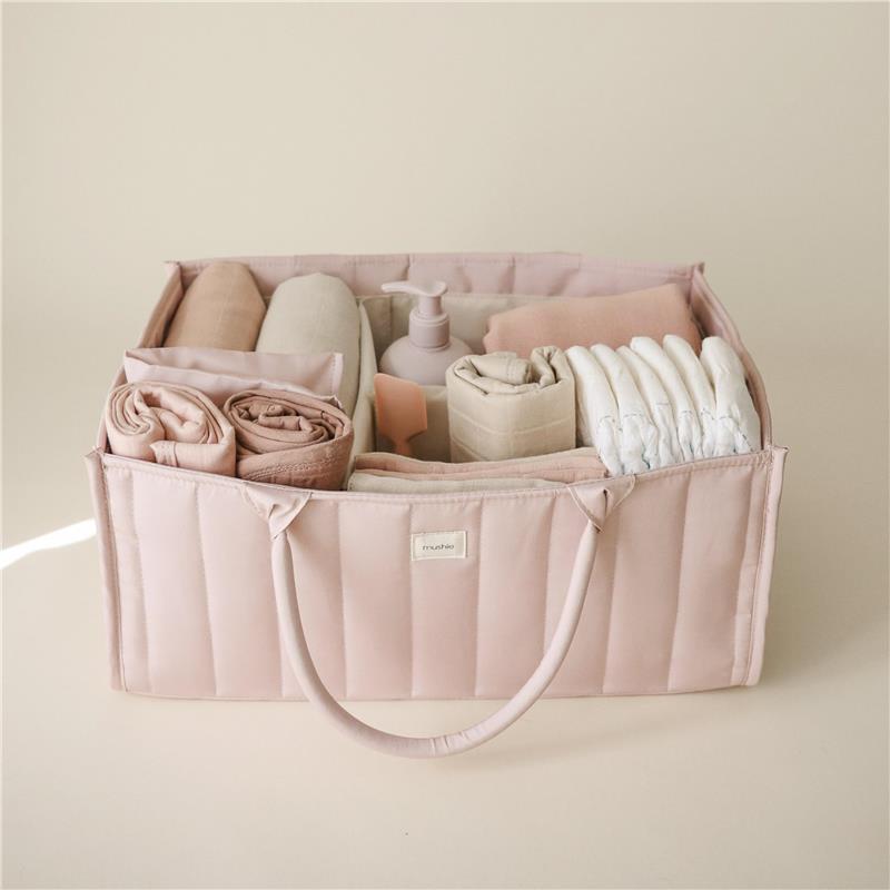 Mushie Baby Diaper Caddy in blush, filled with rolled blankets, diapers, and a lotion bottle, organized for newborn essentials.