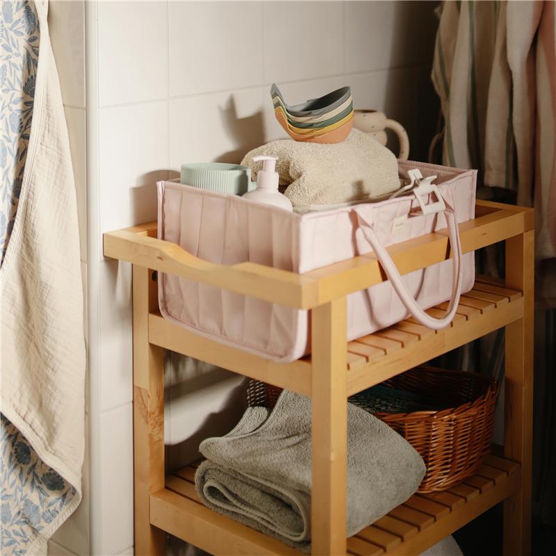 Mushie Baby Diaper Caddy in ivory on a wooden shelf, holding toiletries, a towel, and other newborn essentials.