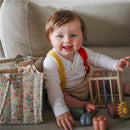 A cheerful baby sits on a sofa with a pastel floral diaper caddy nearby, playing with colorful toys.