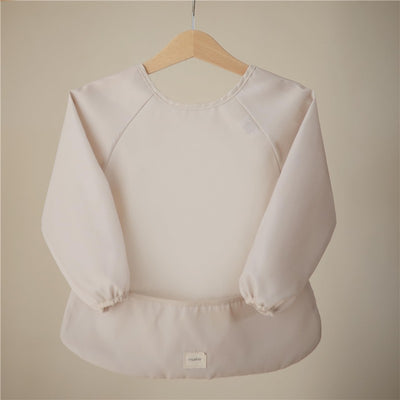 Long sleeve bib in a soft fog color, featuring elastic cuffs and a rounded neckline, hanging against a neutral background.