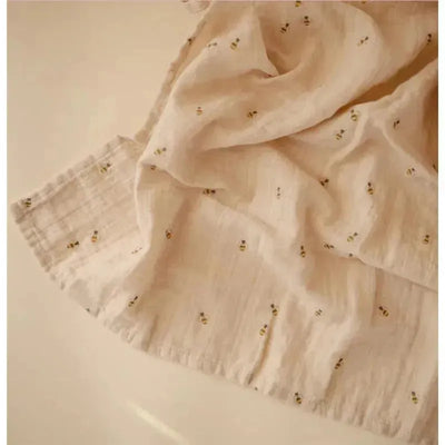 Organic cotton muslin swaddle blanket with a soft beige fabric featuring small bee patterns.