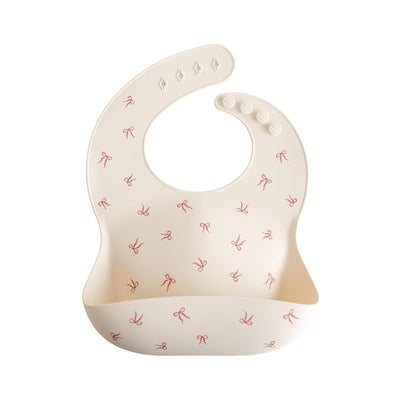Silicone baby bib in cream color with small red bow prints, designed to catch crumbs and spills during mealtime.
