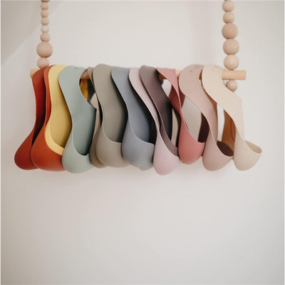 A collection of silicone baby bibs in various colors hanging on a wooden display, showcasing their flexible shapes.
