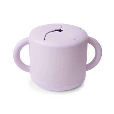 Mushie Silicone Snack Cup in Soft Lilac, featuring a lid with a slit for easy snacking and two handles for grip.