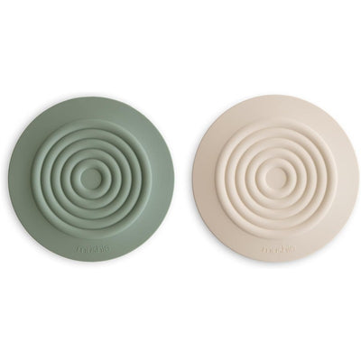 Silicone drain stoppers in dried thyme green and shifting sand beige, featuring concentric circle designs.