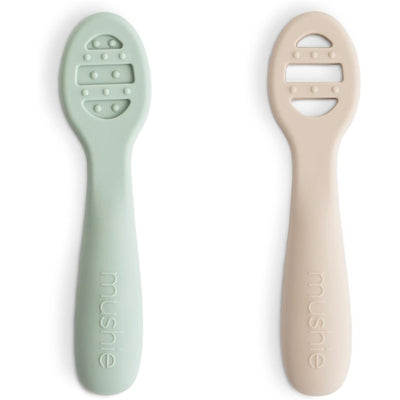 Silicone baby spoons in Cambridge Blue and Shifting Sand colors, designed for first feeding, with a textured grip.