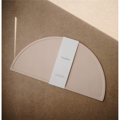 Silicone placemat in blush color with a branded label, placed on a textured surface.