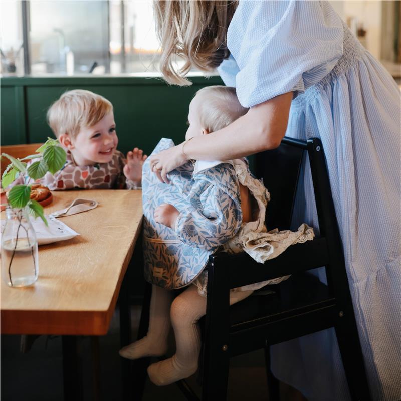 Water-resistant adjustable long sleeve baby bib in a floral design, worn by a seated baby, with a smiling child nearby.