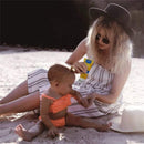 A woman applies Mustela Mineral Sunscreen Lotion SPF 50 to a baby sitting on the sand, both enjoying a sunny day.