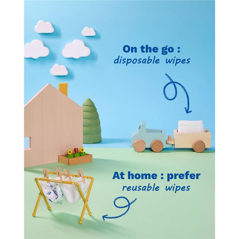 Mustela Compostable Cleansing Water Wipes, displayed with a wooden house and playful props, promote disposable wipes for on-the-go use.