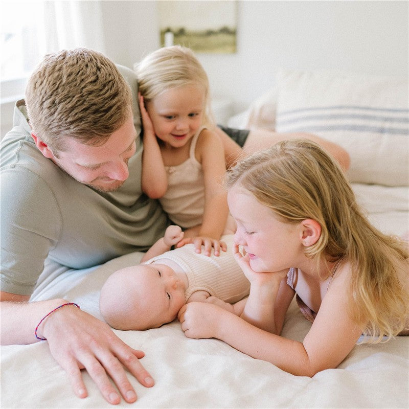 A dad and two young girls interact playfully with a baby on a bed, radiating warmth and family bonding.