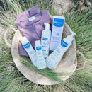 Mustela Newborn Arrival 5-Piece Gift Set in woven basket with lavender baby outfit and skincare products, including diaper rash cream.