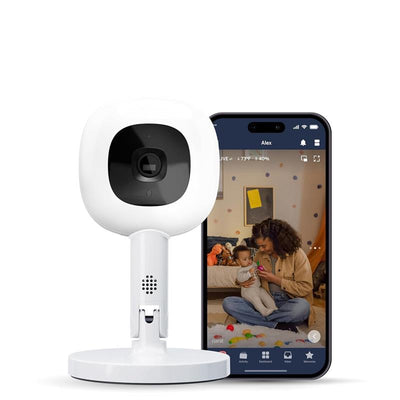Nanit Pro Camera on a stand beside a smartphone displaying a live feed of a parent with a baby.