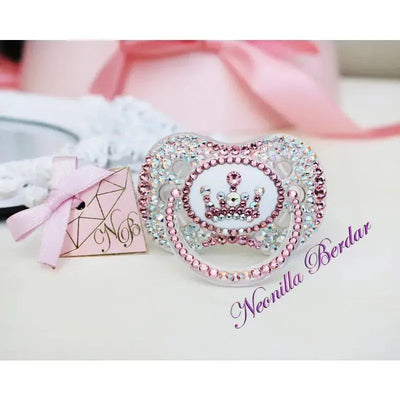 Neonilla Crystal Pacifier featuring a pink bling design with a crown motif and decorative stones, accompanied by a pink ribbon tag.