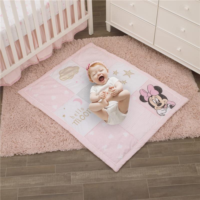 Baby lying on a pink Minnie Mouse-themed play mat featuring cloud, star, and crescent moon designs, smiling joyfully.