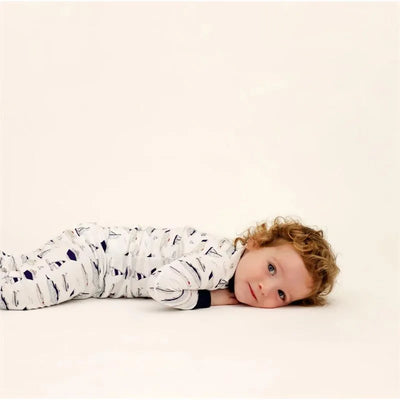 Baby boy lying on stomach, wearing a long sleeve pajama set with boat patterns, smiling at the camera.
