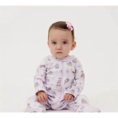 Baby girl seated, wearing a light purple zipper footie adorned with cupcakes and hearts, with a pink bow in her hair.