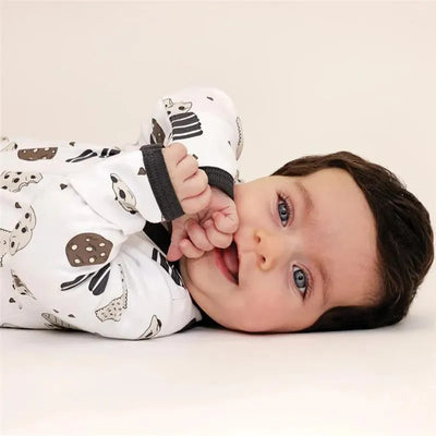 Baby wearing a white Noomie Cookies Zipper Footie with cookie patterns, lying on a light background and smiling.