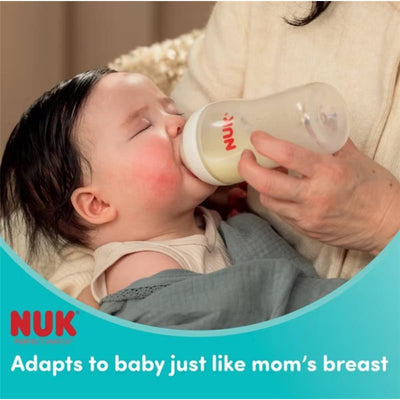 A baby drinking from a Nuk 8 oz baby bottle, held by a caregiver, with the text “Adapts to baby just like mom’s breast” visible.