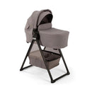 Nuna BMW Swiv stroller with bassinet in Umber color on a black stand, featuring a storage basket underneath.