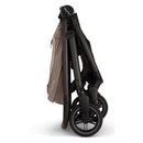 Nuna Swiv stroller folded for travel, featuring a carbon frame with brown fabric and black wheels.