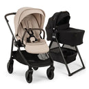 Nuna Swiv stroller in Biscotti color beside a black Swiv bassinet on a stand, showcasing baby gear design and functionality.