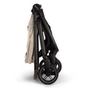 Nuna Swiv Stroller in Biscotti/Caviar color, folded for easy storage, showcasing its sleek design and wheels.