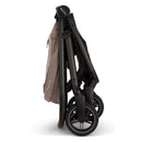 Nuna Swiv stroller in a folded position, featuring a light brown fabric and sleek black frame, with triple wheels.