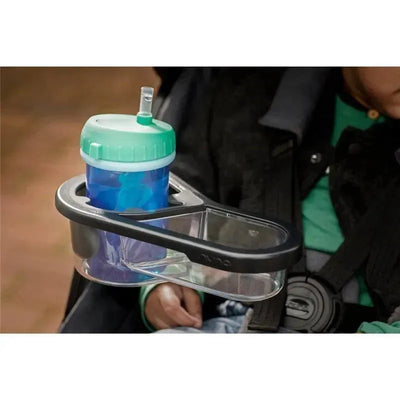 Black Nuna TAVO™ Stroller Child Tray holding a blue cup with a green lid and straw, attached to a stroller.
