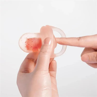 Silicone fruit feeder in lilac held in one hand, with a finger pressing against the food compartment.