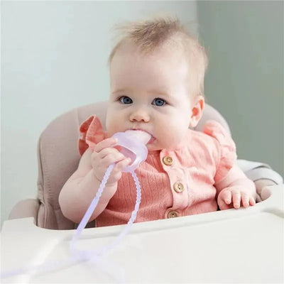 Baby with blue eyes sitting in a high chair, holding a lilac silicone strap and sucking on a teething toy.