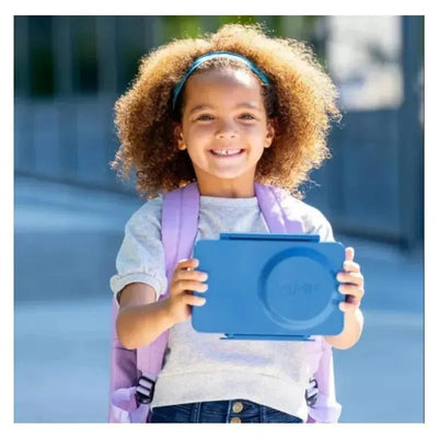 Smiling girl holding an OmieBox in Cosmic Blue, wearing a gray shirt and purple backpack, outdoors.