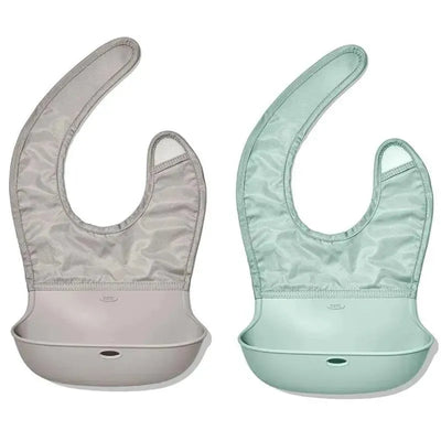 Two silicone bibs from Oxo in opal and drizzle colors, designed for toddlers, featuring a pocket to catch spills.
