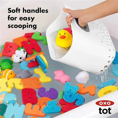 Oxo Tot Stand Up Bath Toy Storage in gray, scooping bath toys like rubber duckies and colorful foam letters from the water.