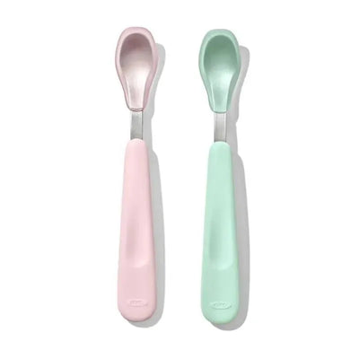 Soft silicone feeding spoon set by OXO, featuring a pink and a mint green spoon with rounded tips.