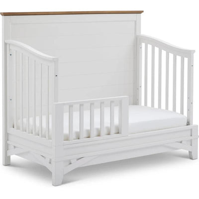 White Parker House Artisan Crib with a wooden top and attached toddler rail, featuring a mattress inside.