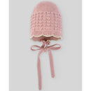 Knit newborn bonnet in powder pink and light brown with a scalloped edge and ties for securing.