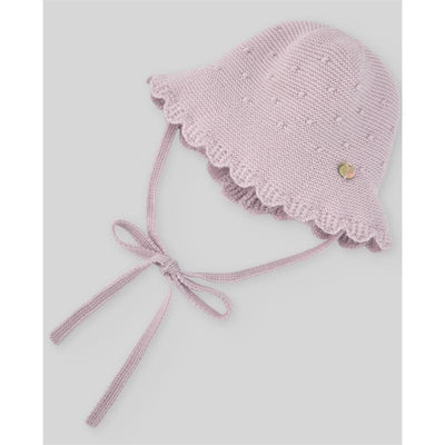 Knit newborn hat in mauve, featuring a scalloped edge and a decorative badge, with ties for secure fitting.