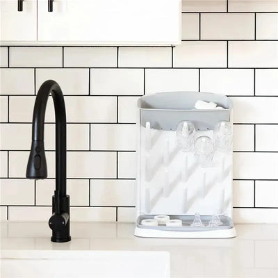 Ubbi Vertical Baby Bottle Drying Rack in gray, featuring multiple slots for drying bottles and accessories, placed on a countertop.